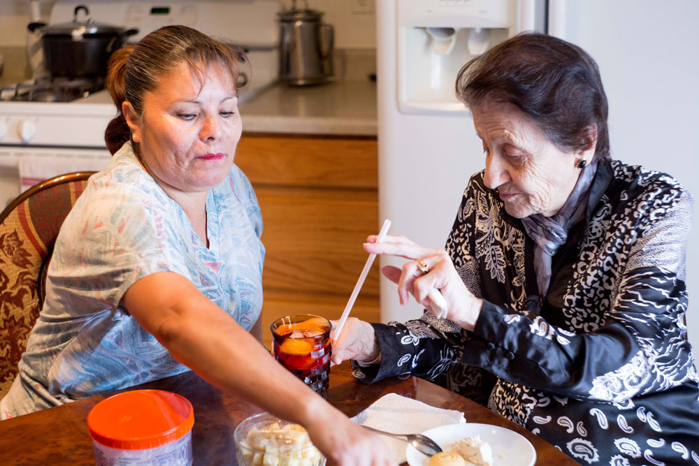 A Home Health Aide assisting an elderly woman with a meal